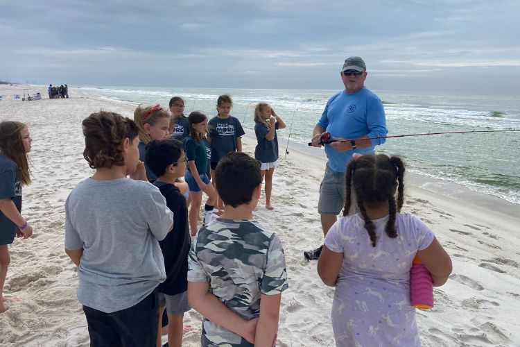 A volunteer teaching children to fish on the beach