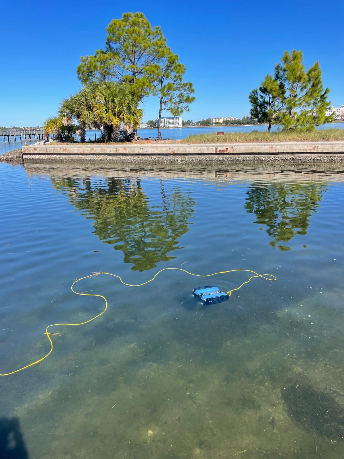 An underwater ROV floating in the clear bay water on its yellow tether