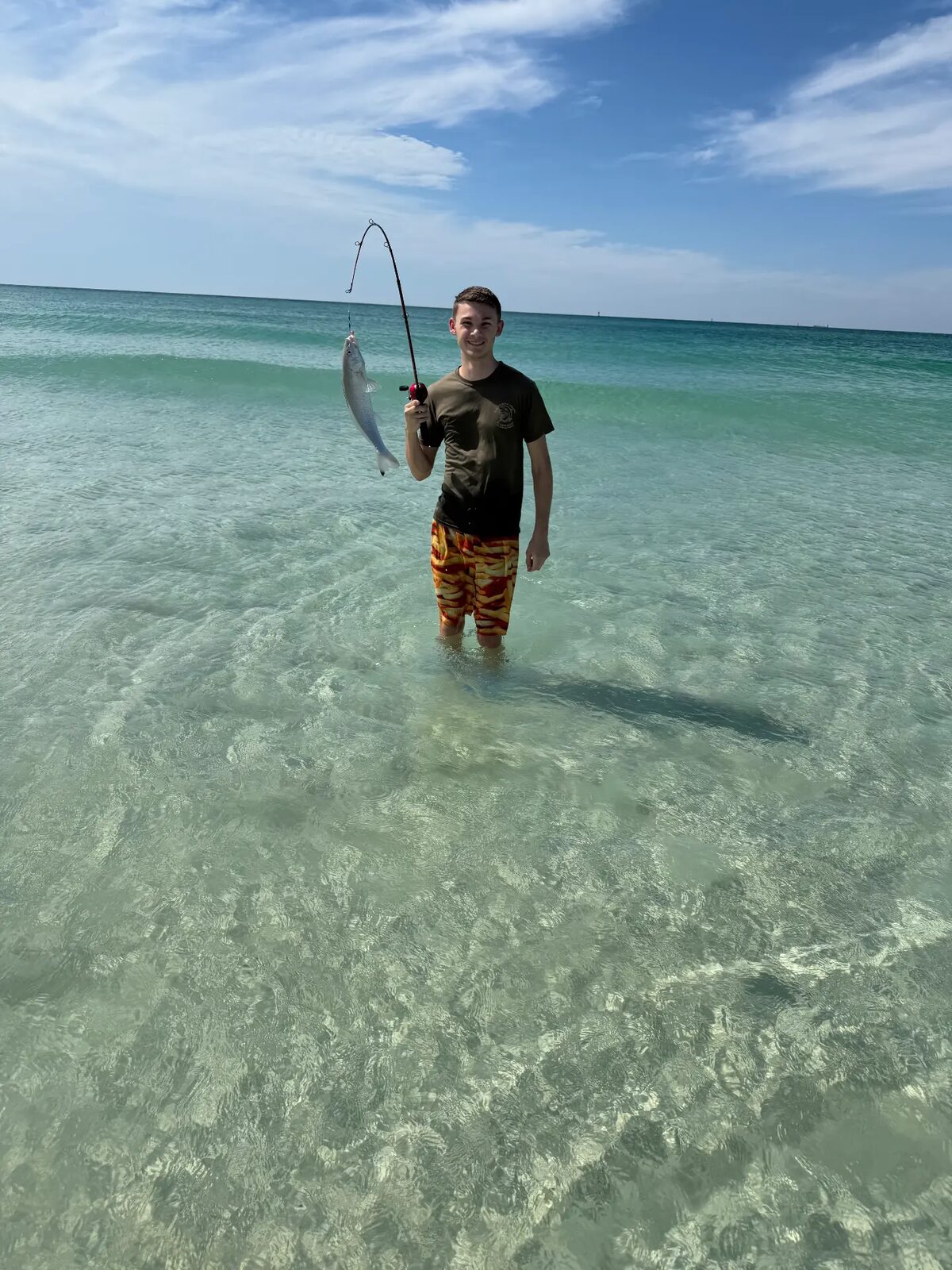 A student holding a fish caught while wading in the Gulf