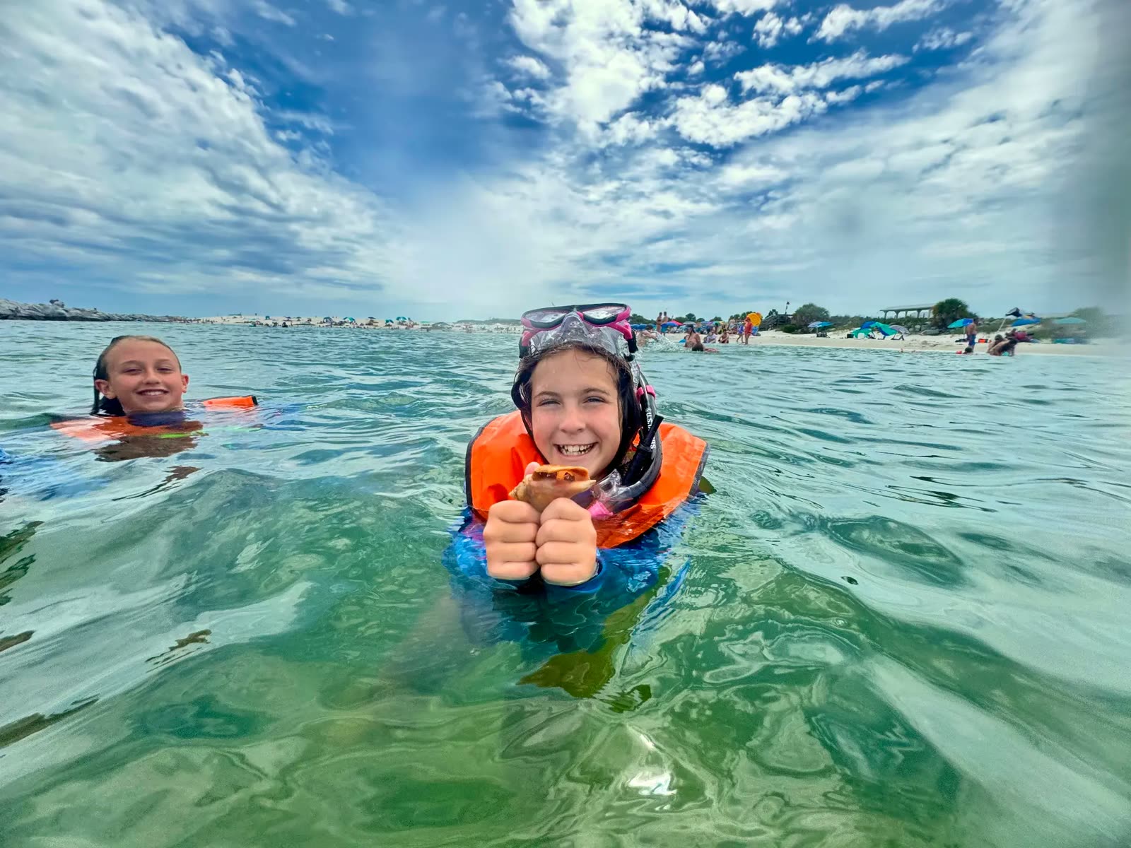 A camper in a wetsuit holding an open sea scallop beside snorkel fins on the beach