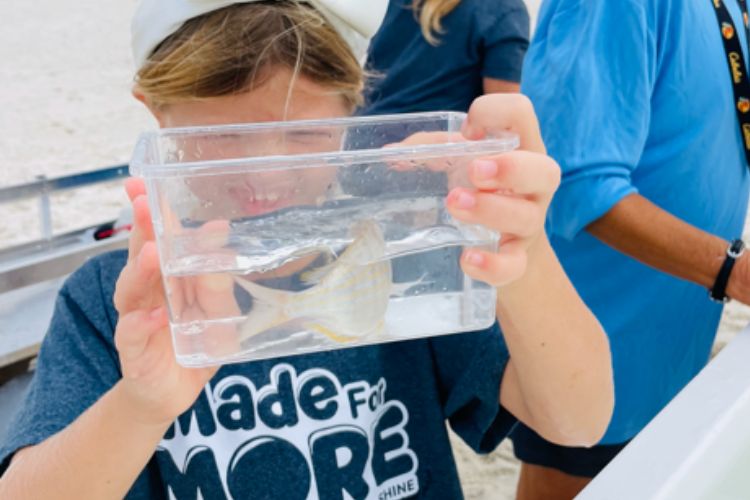 A student holding a clear container with a live fish during a group field program